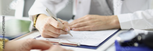 Doctor writing information into documents in front of patient at clinic closeup