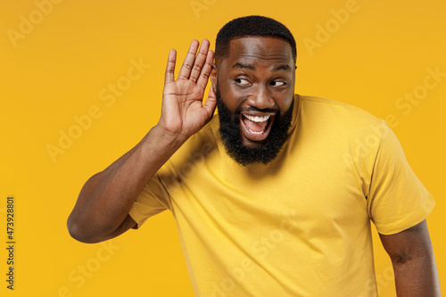Photography Young curious nosy happy black man 20s wearing bright casual t-shirt try to hear you overhear listening intently isolated on plain yellow color background studio portrait