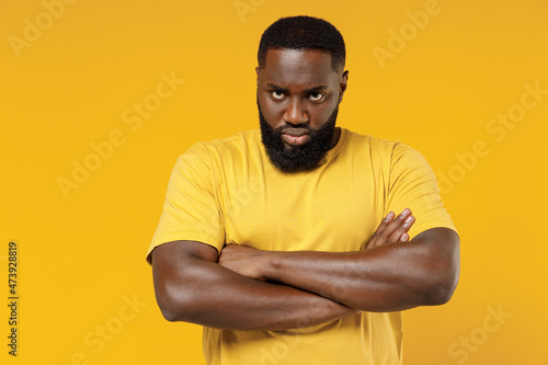 Young angry offended indignant black man 20s wearing bright casual hold hands crossed folded look camera t-shirt isolated on plain yellow color background studio portrait. People lifestyle concept photo