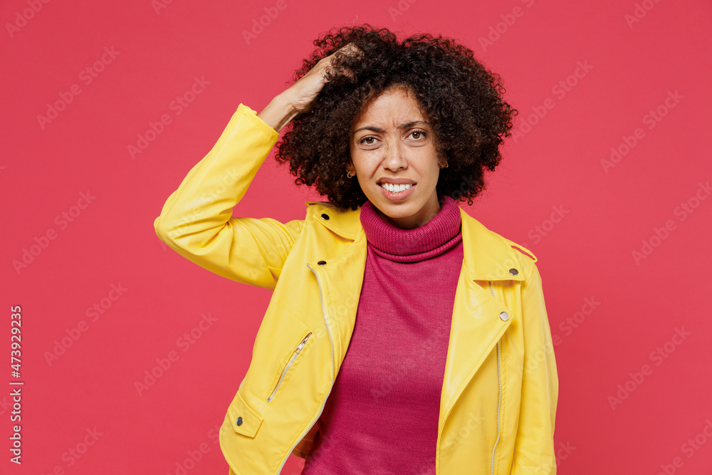 Puzzled pensive thoughtful young curly black latin woman 20s years old wears yellow jacket looking aside rub temple lost in thought and conjectures isolated on plain red background studio portrait. Puzzled pensive thoughtful young curly black latin woman 20s years old wears yellow jacket looking aside rub temple lost in thought and conjectures isolated on plain red background studio portrait.