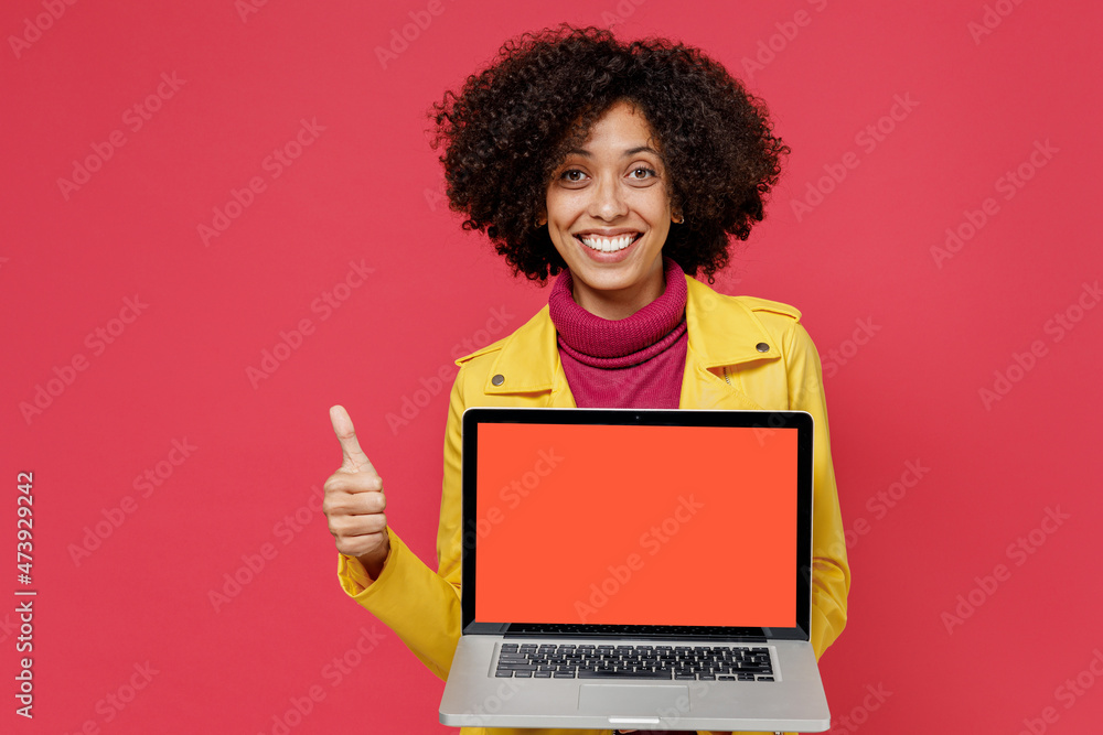 Vivid young black latin woman 20s wears yellow jacket hold use work on laptop pc computer with blank screen workspace area show thumb up like gesture isolated on plain red background studio portrait. Vivid young black latin woman 20s wears yellow jacket hold use work on laptop pc computer with blank screen workspace area show thumb up like gesture isolated on plain red background studio portrait.