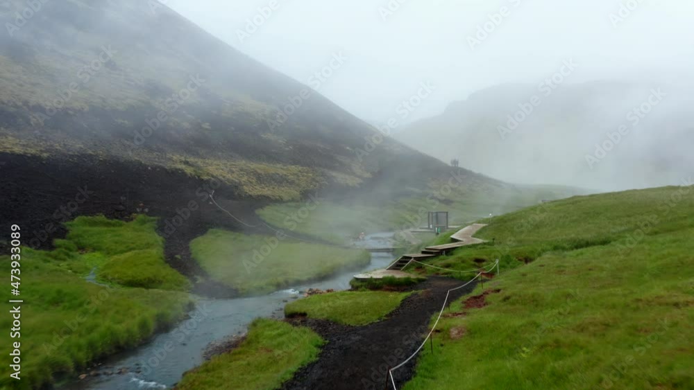 Aerial view of Reykjadalur valley with hot springs river and pool with lush green grass meadow and hills with geothermal steam. Drone view of bathing in thermal hot springs in Iceland