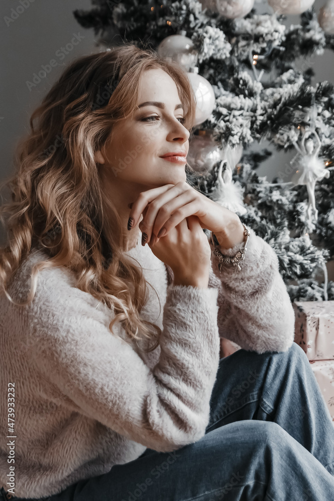 Woman is sitting happy by the christmas tree. Woman is sitting happy by the christmas tree.