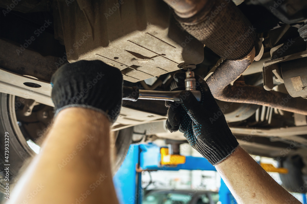 Foto de A car service employee unscrews the oil drain plug in the