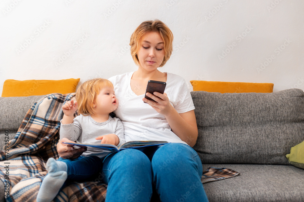 A mother sits with a little child on the couch and uses a smartphone. The kid looks into the smartphone. The concept of family relaxation A mother sits with a little child on the couch and uses a smartphone. The kid looks into the smartphone. The concept of family relaxation