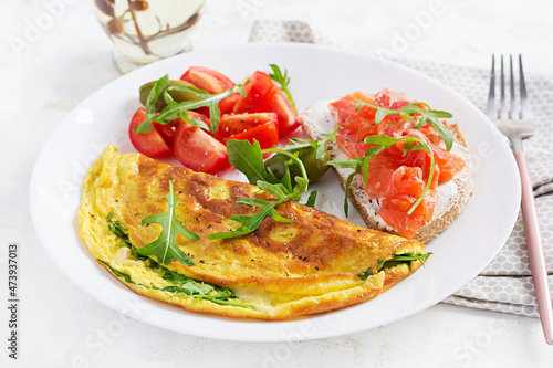 Breakfast. Omelette with cheese, green arugula and sandwich with salmon on white plate. Frittata - italian omelet.