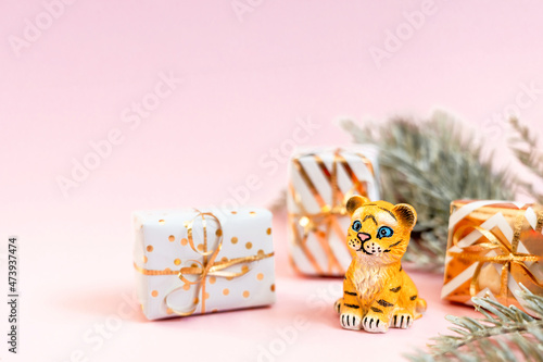 Tiger symbol of the Chinese new year 2022. Figurine of tiger with branches spruce tree and golden gift boxes on pink pastel background. Copy space.