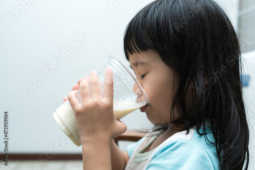 Asian cute girl drinking a glass of milk at home in the morning. The concept is healthy and intelligent kid concept.