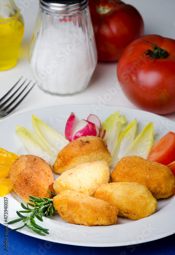 Table set with a plate of croquettes, garnished with tomato, endives, radishes and orange slices.