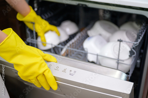 Close-up of a woman housewife wearing gloves to wash dishes using an automatic dishwasher