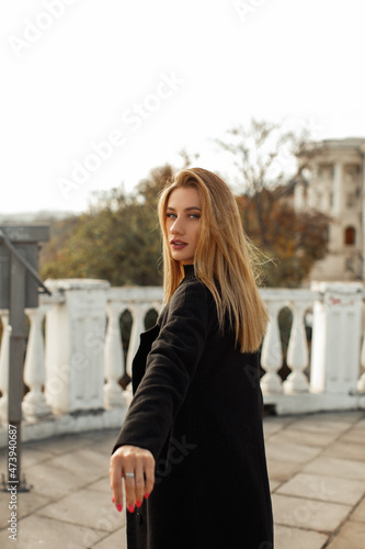 A young beautiful woman in a black coat walks around the city