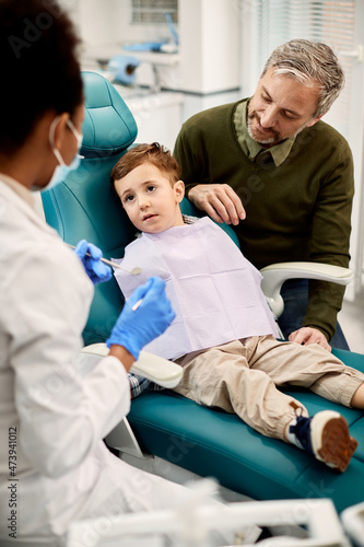 Little boy and his father talk to dentist during teeth check-up at dental clinic.