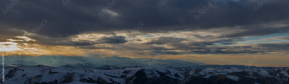 The setting sun illuminates the mountain range through the clouds