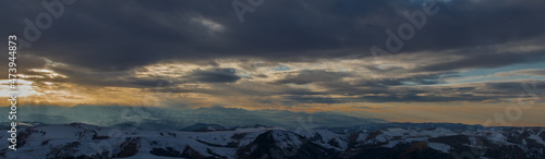 The setting sun illuminates the mountain range through the clouds © Aleksandr