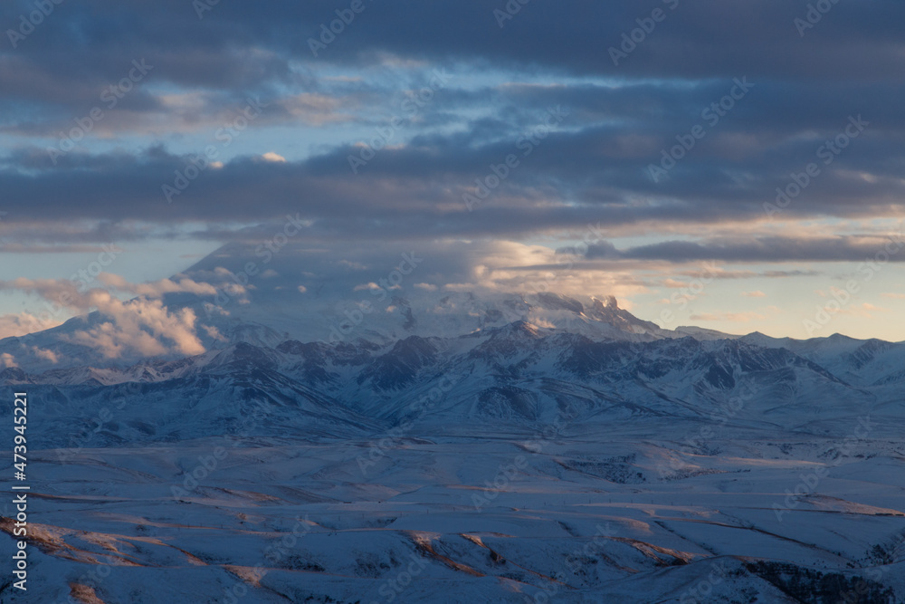 Elbrus in the clouds in the light of the sunset rays