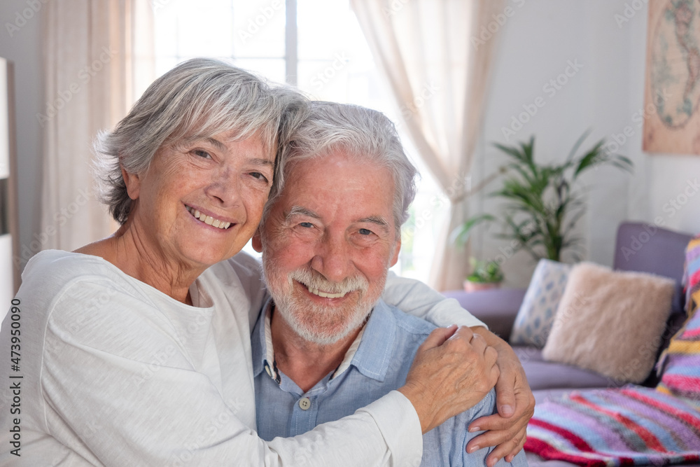 Smiling senior couple sitting at home hugging and looking at camera Smiling senior couple sitting at home hugging and looking at camera