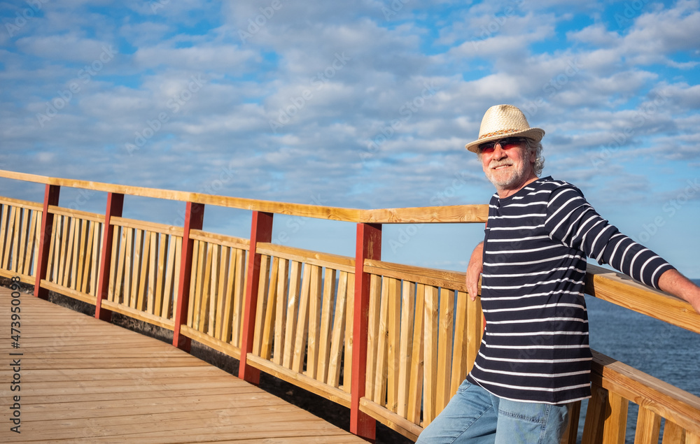 Smiling senior man relaxing in outdoors at sea leaning at a wooden rail. Blue sky and horizon over water Smiling senior man relaxing in outdoors at sea leaning at a wooden rail. Blue sky and horizon over water