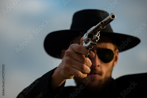 Cowboy shooter in black suit and cowboy hat. Serious man with wild west guns, retro pistol revolver and marshal ammunition. American western Sheriff. Wild west wanted concept.