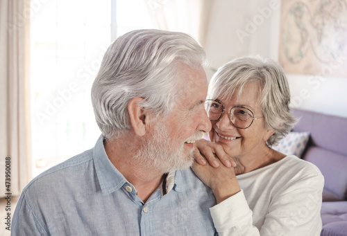 Portrait of beautiful senior couple sitting at home in living room smiling looking each other in the eyes