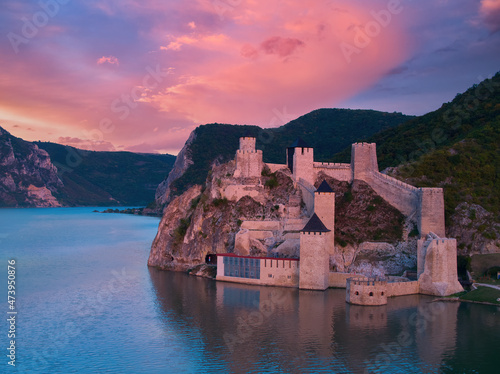 Aerial, iew of the medieval fortress Golubac over  Danube river. Fortress towers illuminated by pink light. Sunset, pink and red clouds sky. Outdoor and traveling castle theme. Serbia. photo