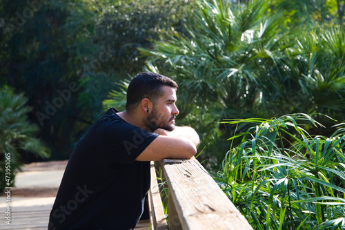 Photography A gay man of Latin origin, dark and bearded, stands pensively looking nowhere in the park