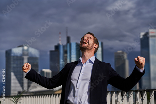 Happy male professional with eyes closed making fists while celebrating success on rooftop photo