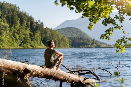 Man looking at view while siting on fallen tree at lake photo