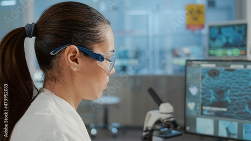 Biology specialist working with computer to examine dna animation in laboratory. Microbiologist with protective glasses using lab equipment to work on scientific experiment for innovation.