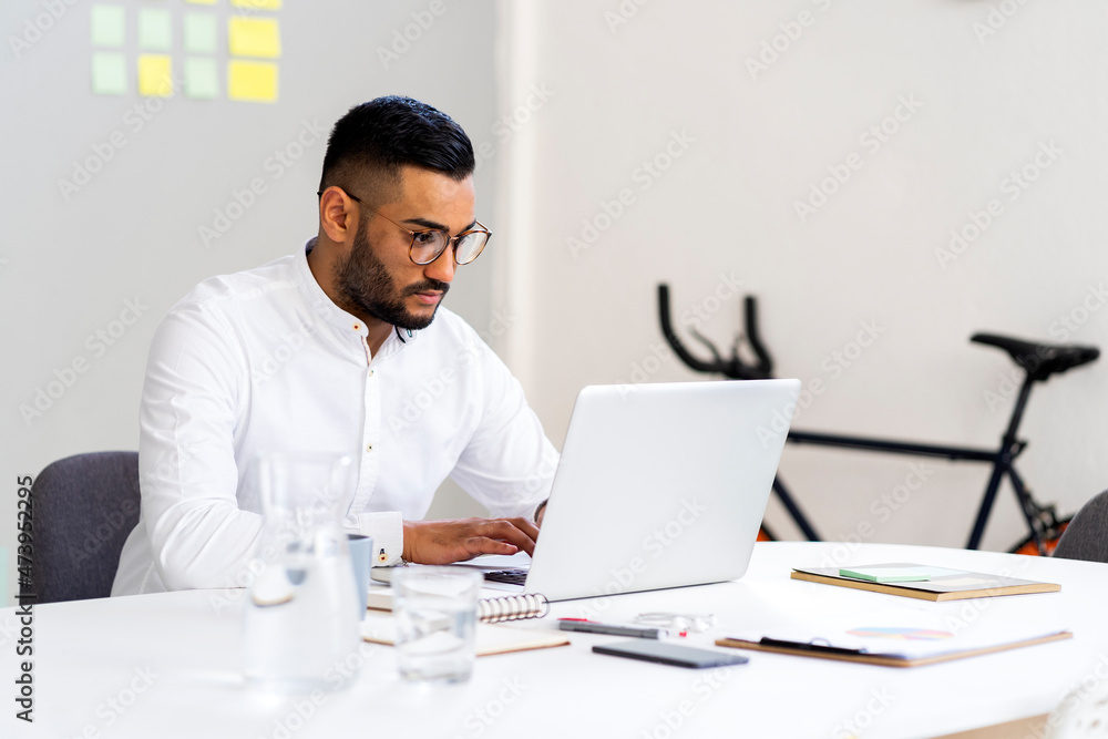 Male entrepreneur using laptop on desk while working at office Male entrepreneur using laptop on desk while working at office