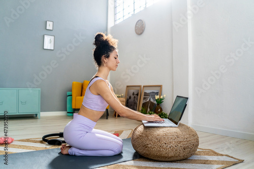 Woman using laptop on hassock while kneeling at home photo