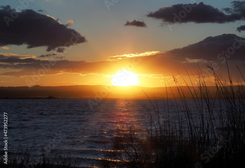 Sunset over the lake. The sun sets behind the mountain against the backdrop of lake water and reeds. Very beautiful landscape for wallpaper  posters and screensavers