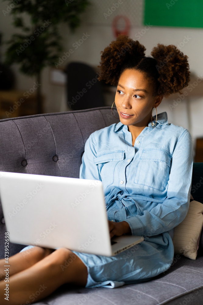 Young woman sitting with laptop on sofa while contemplating in living room Young woman sitting with laptop on sofa while contemplating in living room