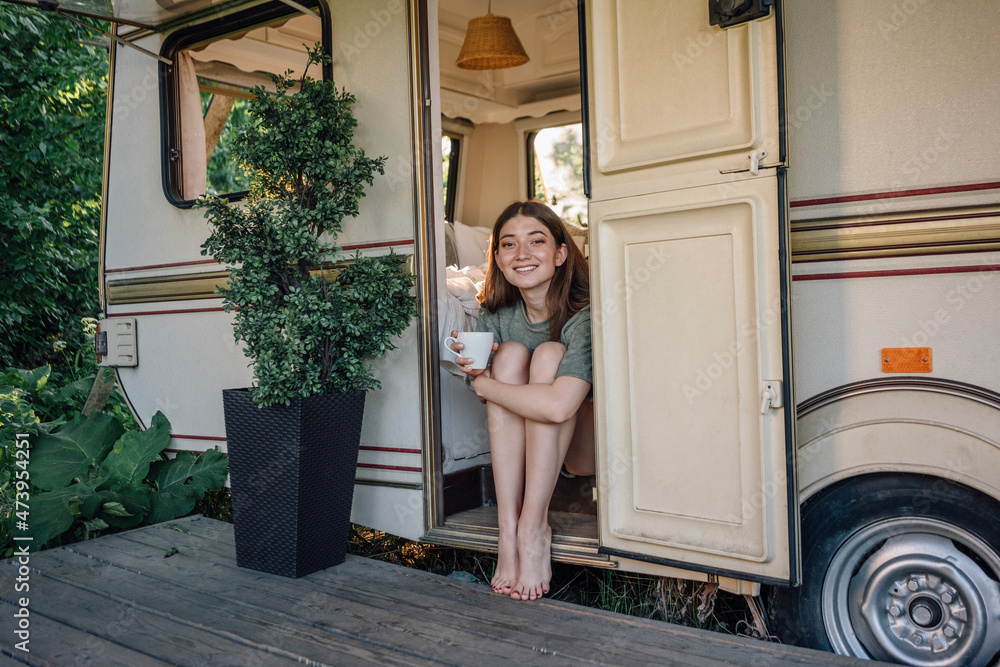 Smiling beautiful woman holding coffee cup sitting at camper doorway Smiling beautiful woman holding coffee cup sitting at camper doorway