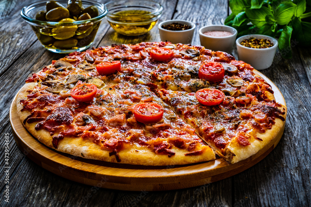 Pizza capricciosa with mozzarella, white mushrooms, ham and tomatoes on wooden table
