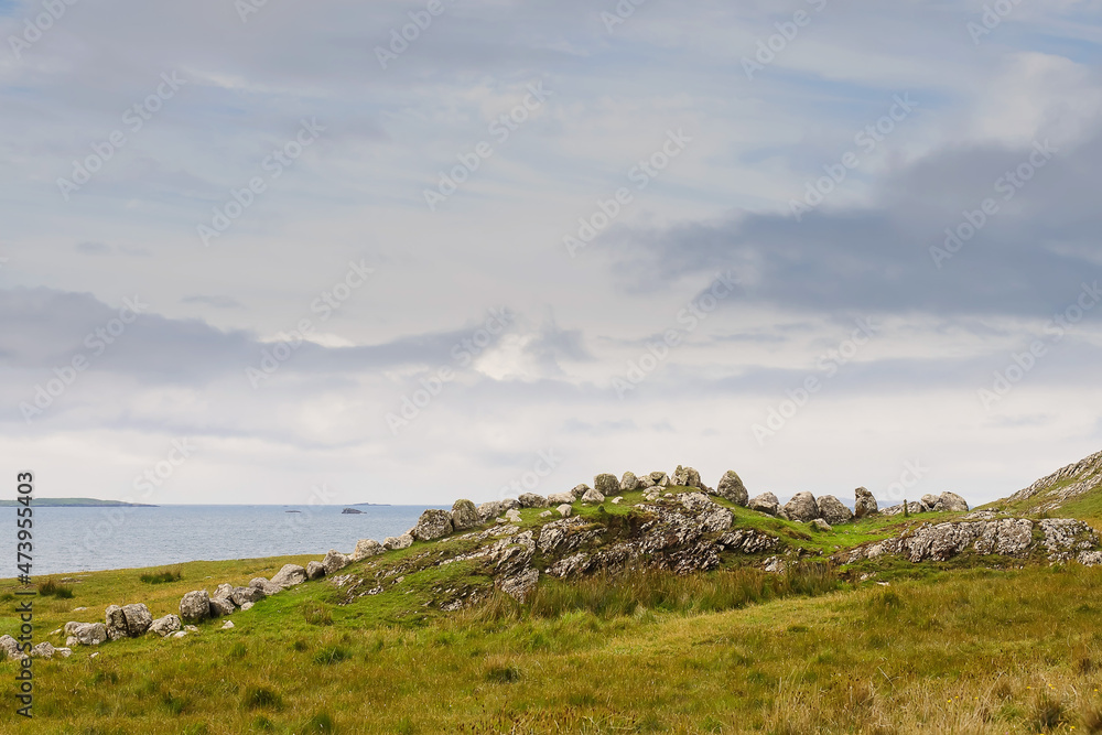 Stones on a hill resemble sleeping dragon, Ocean and pastel blue cloudy sky in the background. Landscape scene in county Mayo, Ireland.