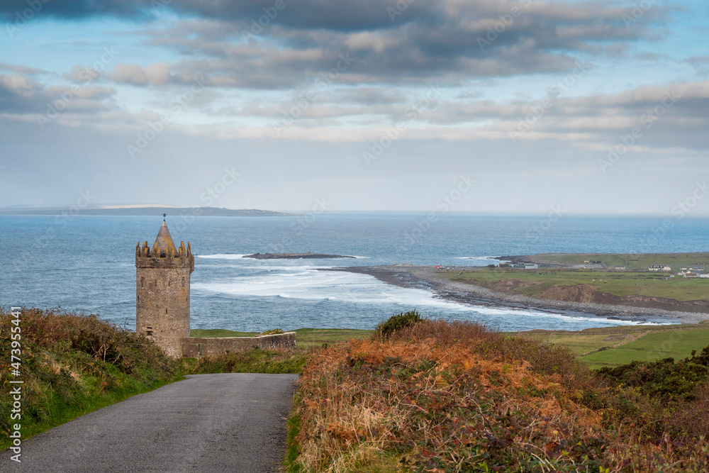 Small road leads to Doonagore castle, Doolin pier and Aran islands in the background. Beautiful cloudy sky. Popular tourist attraction in county Clare, Ireland. Fine example of old fortress.