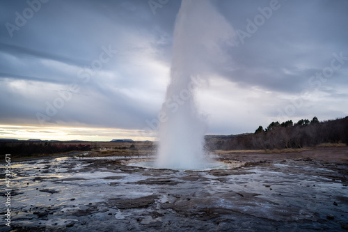 Eruption of Strokkur geyser in Iceland. Winter cold colors, sun lighting through the steam