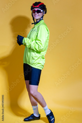 Cycling Ideas. Full Length Portrait of Confident Positive Female Road Cyclist in Professional Outfit Standing In Green Autumn Jacket Against Yellow © danmorgan12