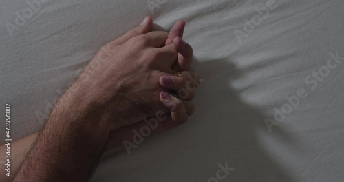 A close-up of the hands of an unrecognizable man and woman making love on a white sheet. Romance and humiliation concept