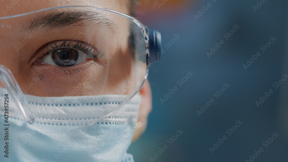 Scientist showing one eye on camera in laboratory, wearing safety glasses  and face mask. Woman biologist looking at camera with face of face, working  in research lab. Close up Stock Photo