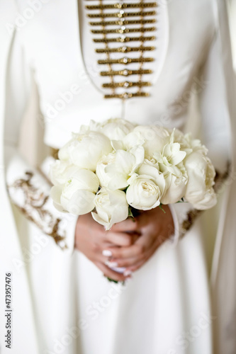 a girl in a wedding national Caucasian dress holds a wedding bouquet of white peonies photo