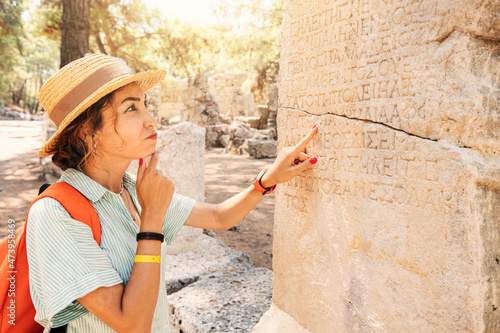 Woman philologist and tourist reads and tries to translate ancient Greek from columns in the ruins of an antique city. Linguistics and archaeology photo