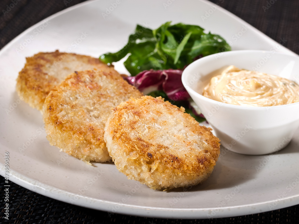 portion of chicken patties on a plate served with salad mix and sauce thousand island, photo on dark background portion of chicken patties on a plate served with salad mix and sauce thousand island, photo on dark background