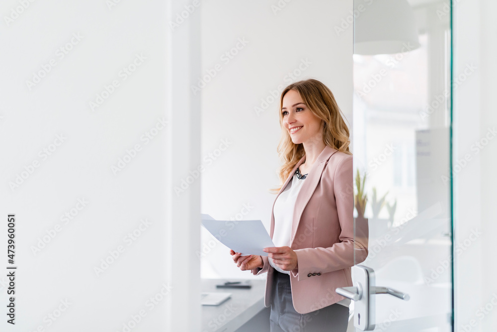 Female professional with document day dreaming while standing in office Female professional with document day dreaming while standing in office