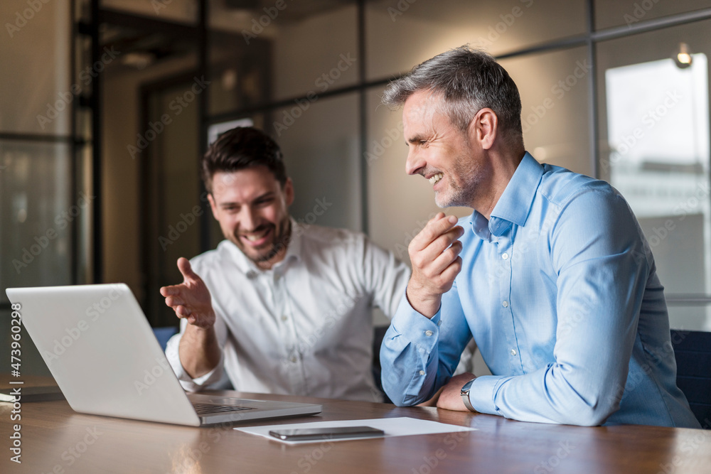 Smiling male professionals discussing over laptop in board room Smiling male professionals discussing over laptop in board room