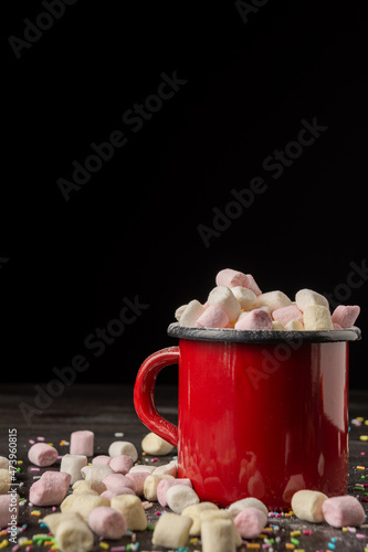Top view of red mug with marshmallows, on dark table, selective focus, black background, vertical, with copy space
