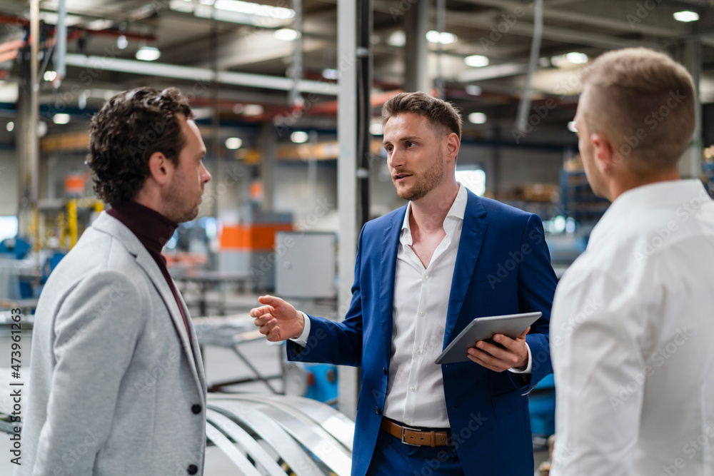 Businessman holding digital tablet while discussing with colleagues at industry Businessman holding digital tablet while discussing with colleagues at industry