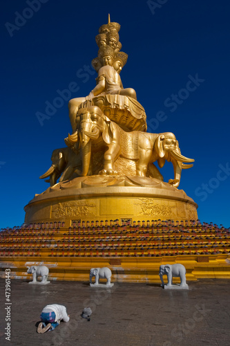 China, Sichuan, Emeishan City, Person praying in front of golden statue of Samantabhadra at summit of Mount Emei photo