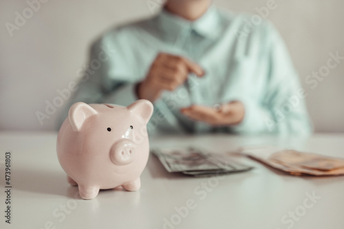 Business woman counts dollar banknotes money. Pink piggy bank with a coin on the table