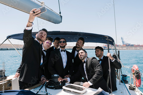 Man taking selfie with male friends through mobile phone in yacht photo